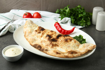 Delicious calzone served with sauce on grey table