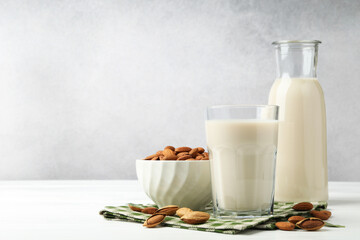 Fresh nut milk and almonds on white wooden table, space for text