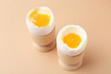 Soft boiled eggs in cups on beige background, closeup