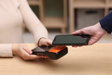 Woman paying with smartphone via terminal at wooden counter indoors, closeup