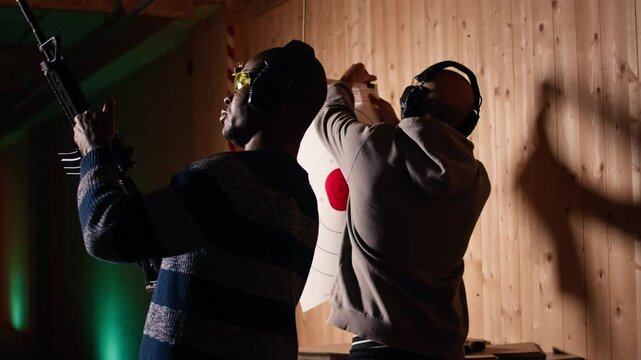 Man holds rifle, enjoying recreational shooting experience in firing range next to group of friends. People practicing with weapons in safe environment at shooting range company, camera A