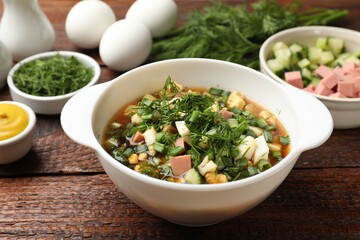 Delicious okroshka soup and ingredients on wooden table, closeup