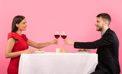 Romantic Date. Lovely Couple Clinking Glasses Drinking Wine Sitting At Restaurant Table Over Yellow Background. Studio Shot