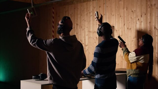 Company coworkers enjoying recreational shooting experience in firing range during teambuilding. Workplace colleagues practicing with weapons in safe shooting range environment, camera A