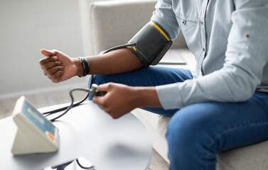 Obraz premium Unrecognizable African Guy Measuring Arterial Pressure Having Hypertension Sitting On Sofa At Home. Cropped. Health Problem With Low And High Blood Tension, Blood-Pressure Checkup. Selective Focus