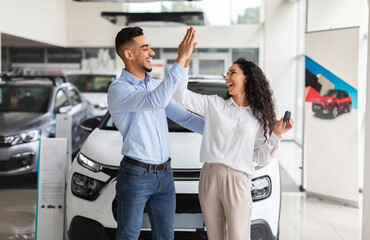 Emotional middle-eastern lovers young man and woman giving high five, standing by nice brand new...