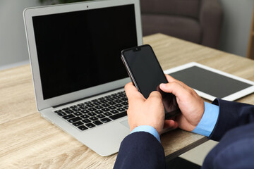 Businessman using smartphone near laptop at wooden table, closeup. Modern technology