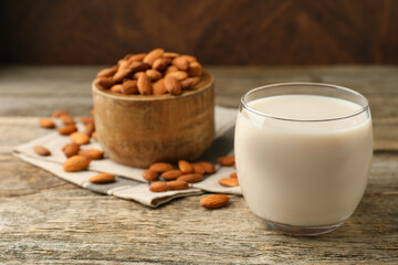 Fresh almond milk in glass and nuts on wooden table, closeup