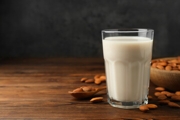 Fresh almond milk in glass and nuts on wooden table, space for text