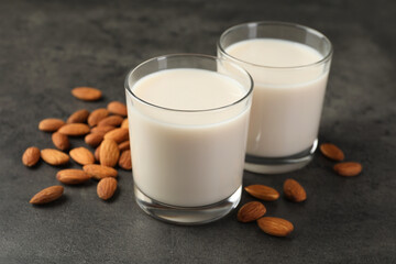 Fresh almond milk in glasses and nuts on dark grey table, closeup