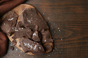 Pieces of chocolate with salt on wooden table, top view. Space for text