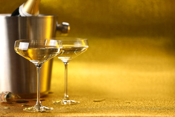 Champagne in glasses and ice bucket with bottle on golden background. Space for text