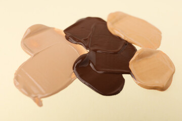 Samples of different foundations on beige background, closeup