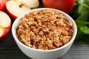 Delicious apple crisp in bowl, fresh fruits and mint on black textured table, closeup