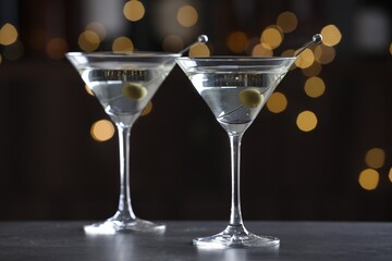 Martini cocktail with olives in glasses on grey table against blurred background, closeup. Bokeh effect