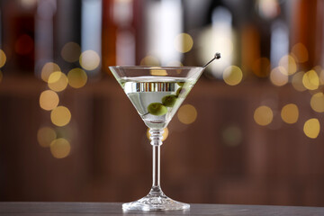 Martini cocktail with olives in glass on wooden table against blurred background. Bokeh effect