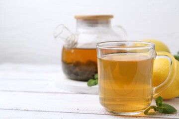 Aromatic mint tea with lemons and fresh leaves on white wooden table, closeup. Space for text