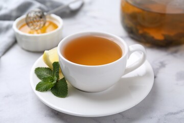 Aromatic mint tea in cup, fresh leaves and lemon on light marble table, closeup