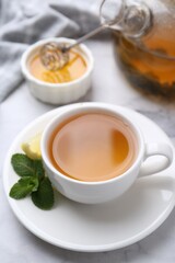 Aromatic mint tea in cup, fresh leaves, lemon and honey on light table, closeup
