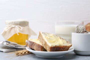 Slices of bread with butter, honey, milk and spike on light grey table, closeup