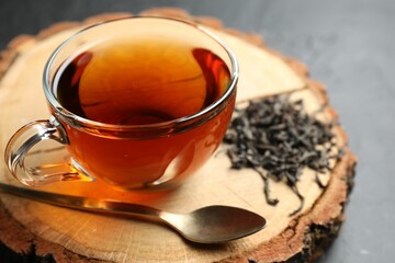 Aromatic black tea in cup and dry leaves on grey table, closeup
