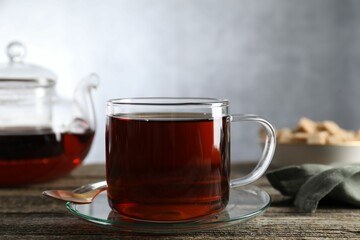 Aromatic black tea in cup and spoon on wooden table, closeup