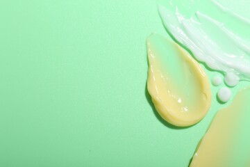 Cream samples on light green background, top view. Space for text