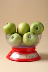 Kitchen scale with apples on beige background, closeup