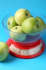 Kitchen scale with apples on light blue background, closeup