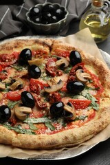 Tasty pizza with mushrooms, olives and arugula on black table, closeup