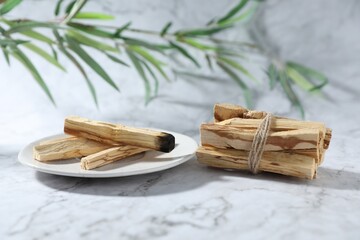 Palo santo sticks, burnt one and green branch on white marble table, closeup