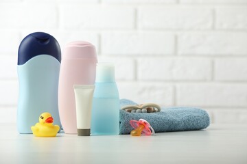 Baby cosmetic products, pacifier, towel and rubber duck on table against white brick wall. Space for text