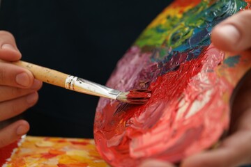 Man with palette and paintbrush drawing picture, closeup