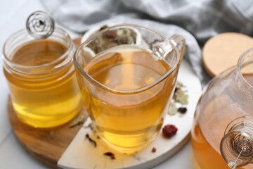 Delicious herbal tea with honey and dry leaves on white table, closeup