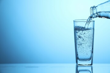 Pouring soda water from bottle into glass on light blue background, closeup. Space for text