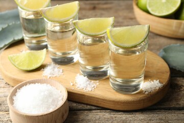 Tequila shots with lime slices, salt and agave leaves on wooden table, closeup