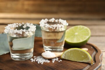 Tequila shots with salt, lime slices and agave leaves on wooden table, closeup
