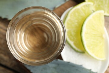 Tequila shot with lime slices, salt and agave leaves on wooden table, flat lay