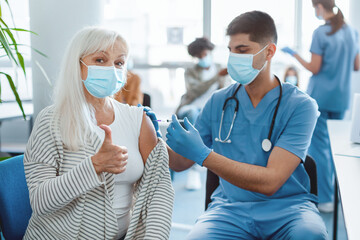 Successful flu Vaccination Concept. Senior Woman In Face Mask Gesturing Thumb Up While Getting...