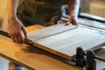 Unrecognizable woodworker hands hold glued tabletop, clamping several boards in one piece with clamps on machine in furniture workshop. Master hands apply clamps to secure boards into one piece