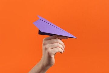 Woman with purple paper plane on orange background, closeup