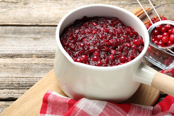 Tasty cranberry sauce in saucepan and berries on wooden table, closeup