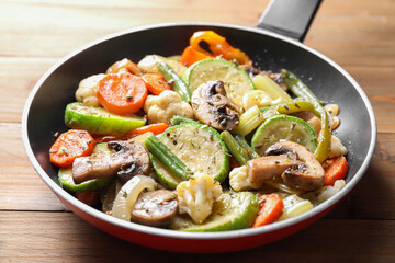 Different vegetables and mushrooms in frying pan on wooden table, closeup