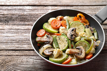 Different vegetables and mushrooms in frying pan on wooden table, closeup