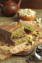 Pieces of Dubai chocolate bar with pistachios, knafeh and cacao chips on wooden table, closeup