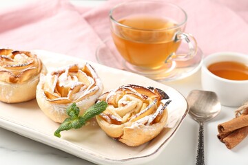 Freshly baked apple roses with mint, honey, cinnamon sticks and tea on white marble table, closeup