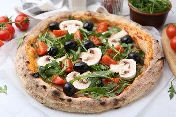 Tasty pizza with cherry tomatoes, black olives, mushrooms and arugula on white tiled table, closeup