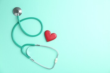 Fototapeta premium Cardiology. Stethoscope and red decorative heart on turquoise background, flat lay. Space for text