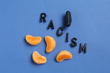 Word Racism and tangerine segments of different colors on blue background, flat lay