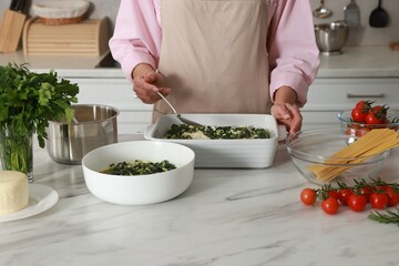 Woman making spinach lasagna at marble table in kitchen, closeup